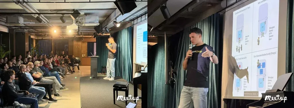 A speaker presents to an attentive audience, standing beside a projector screen displaying diagrams